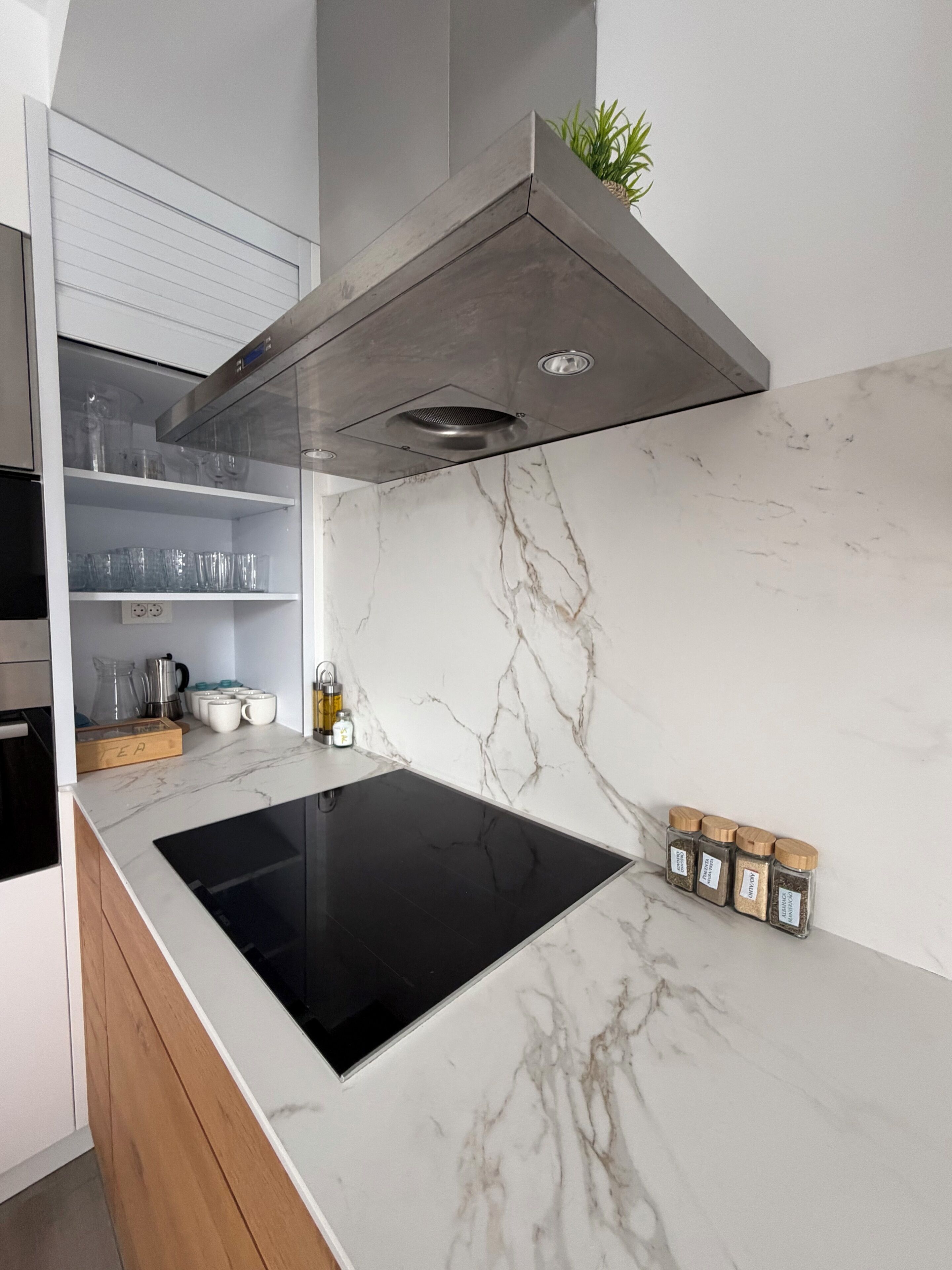 A modern kitchen with a black induction cooktop, marble backsplash, and built-in cabinets.