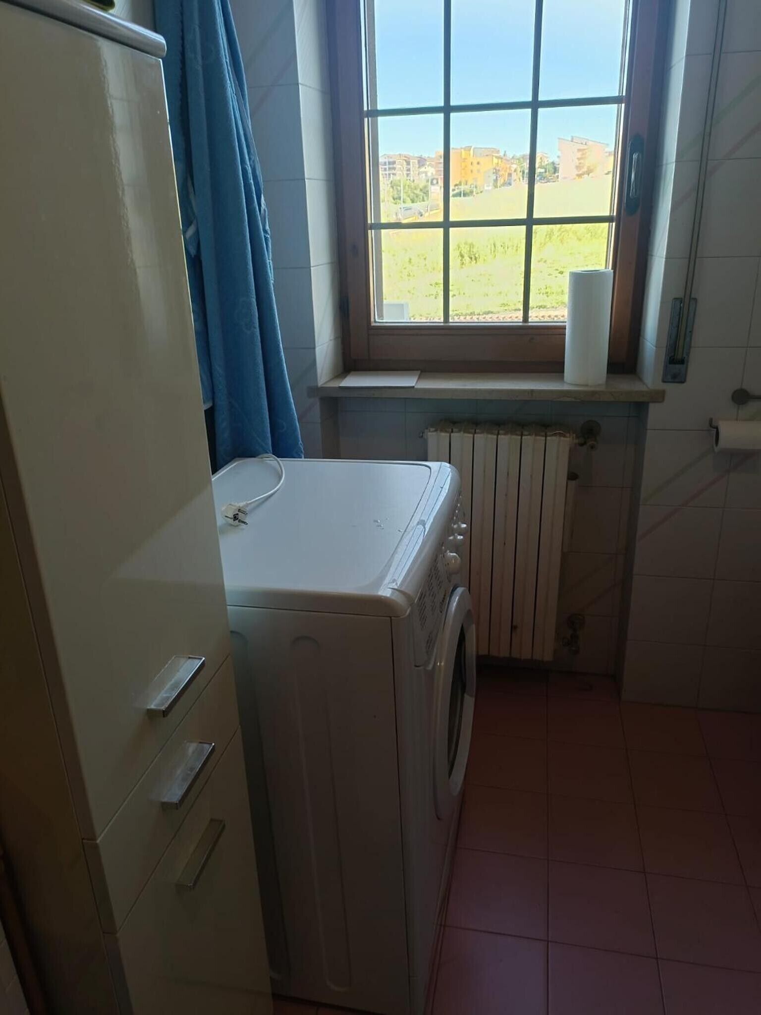 Een wasserette met een wasmachine, een droger, een raam met uitzicht en een radiator.