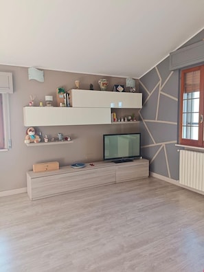 Una habitación con un televisor sobre un mueble bajo, un estante inferior con objetos decorativos y una pared con diseño.