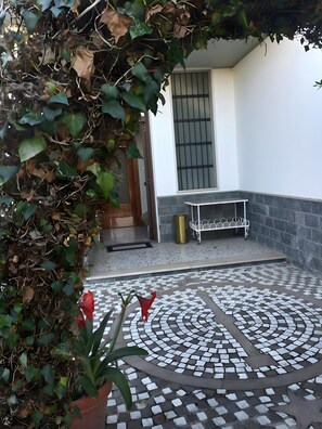 Une terrasse carrelée avec un banc, un pot de fleurs et une porte donnant sur une pièce.