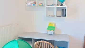 Un área de juegos infantil con una carpa verde, una silla de mimbre y estantes con juguetes y un globo terráqueo.