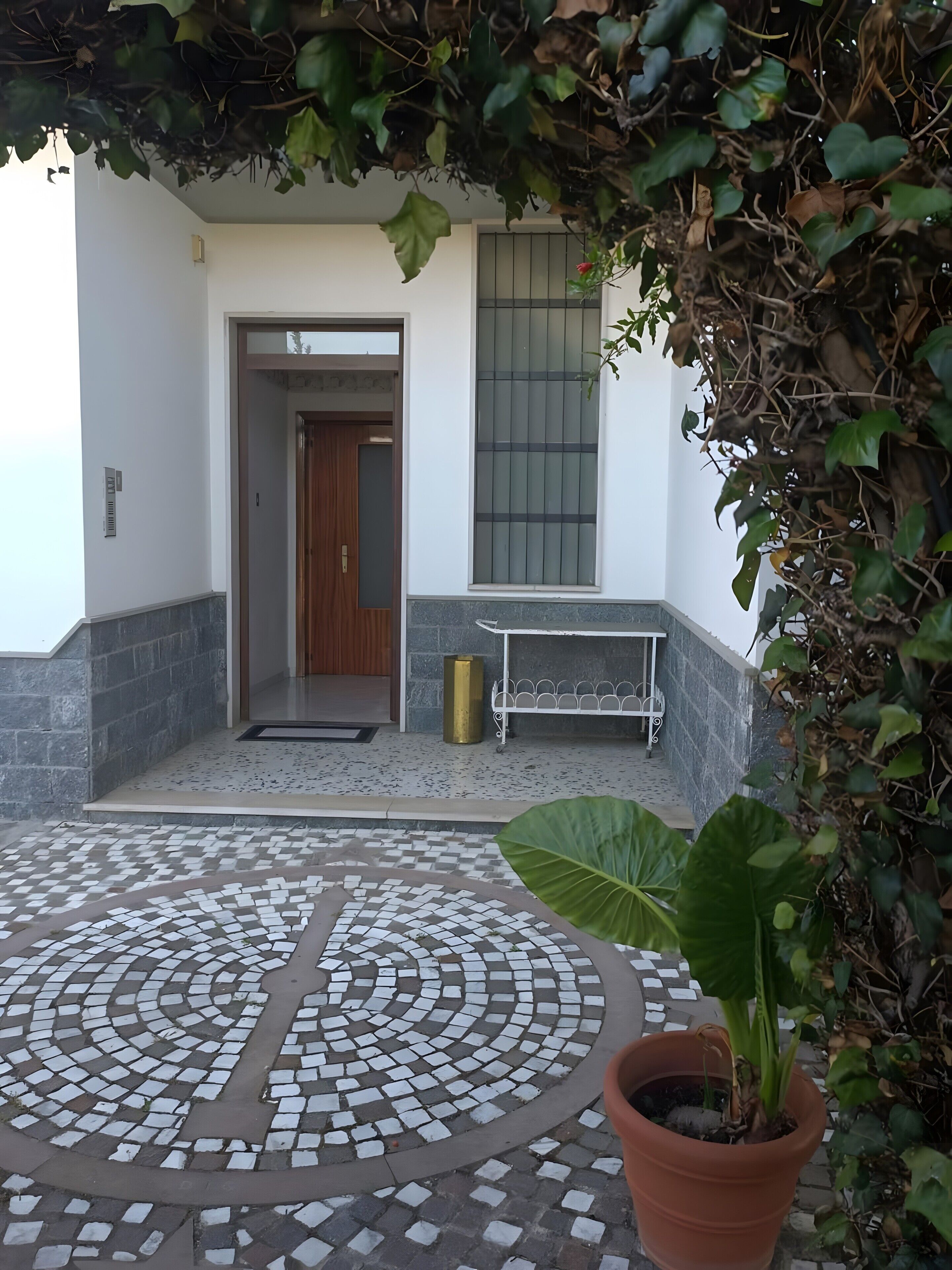 Une cour dallée avec un pot de fleurs, un banc et une porte donnant sur un espace intérieur.