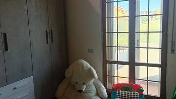A room with a large wardrobe, a teddy bear, and a window with a view of buildings.