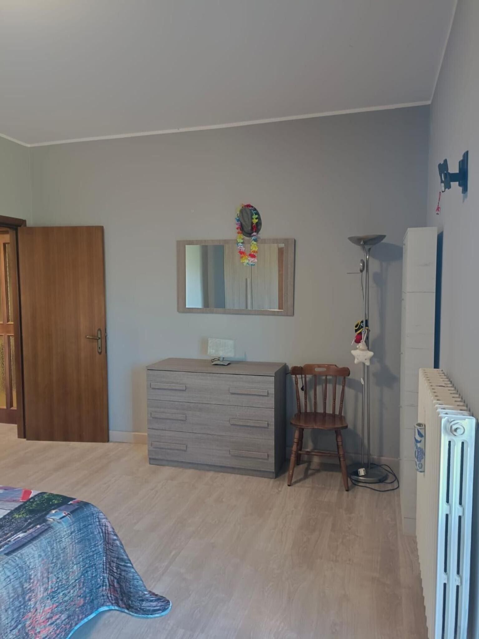 Un dormitorio con cama, tocador, silla, espejo, radiador y puerta.