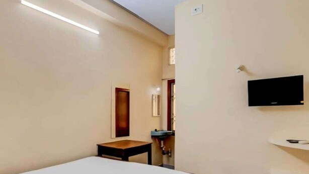 Une chambre d’hôtel avec un lit, une petite table, un téléviseur fixé au mur et un ventilateur de plafond.
