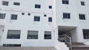 Un immeuble blanc à plusieurs étages, doté d’un toit plat, de grandes fenêtres et d’une entrée couverte avec un escalier.