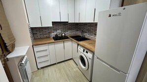 Una cocina compacta con armarios blancos, lavadora incorporada y refrigerador.