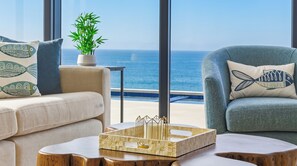Ein modernes Wohnzimmer mit Meerblick, ausgestattet mit einer Couch, einem Sessel und einem Deko-Tablett.