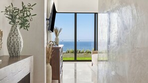 Ein modernes Interieur mit großem Fenster zum Meer, einem wandmontierten Flachbildfernseher und einem minimalistischen Design.