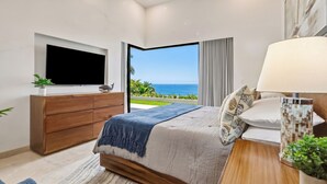 Ein Schlafzimmer mit Bett, Fernseher, Nachttisch mit Lampe und Blick aufs Meer.
