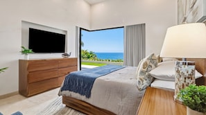 Ein Schlafzimmer mit Bett, Fernseher, Nachttisch mit Lampe und Blick aufs Meer.