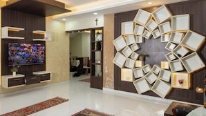 A modern interior with a flat-screen TV, a unique geometric wall art piece, and a cross on the wall. - Grand Villa Kochi (Kanayannur)