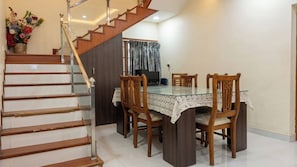 Comedor con una mesa de vidrio, sillas de madera, una escalera y un televisor.
