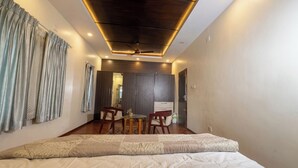 A bedroom with a bed, a ceiling fan, a dining area with chairs and a table, and a wardrobe. - Grand Villa Kochi (Kanayannur)