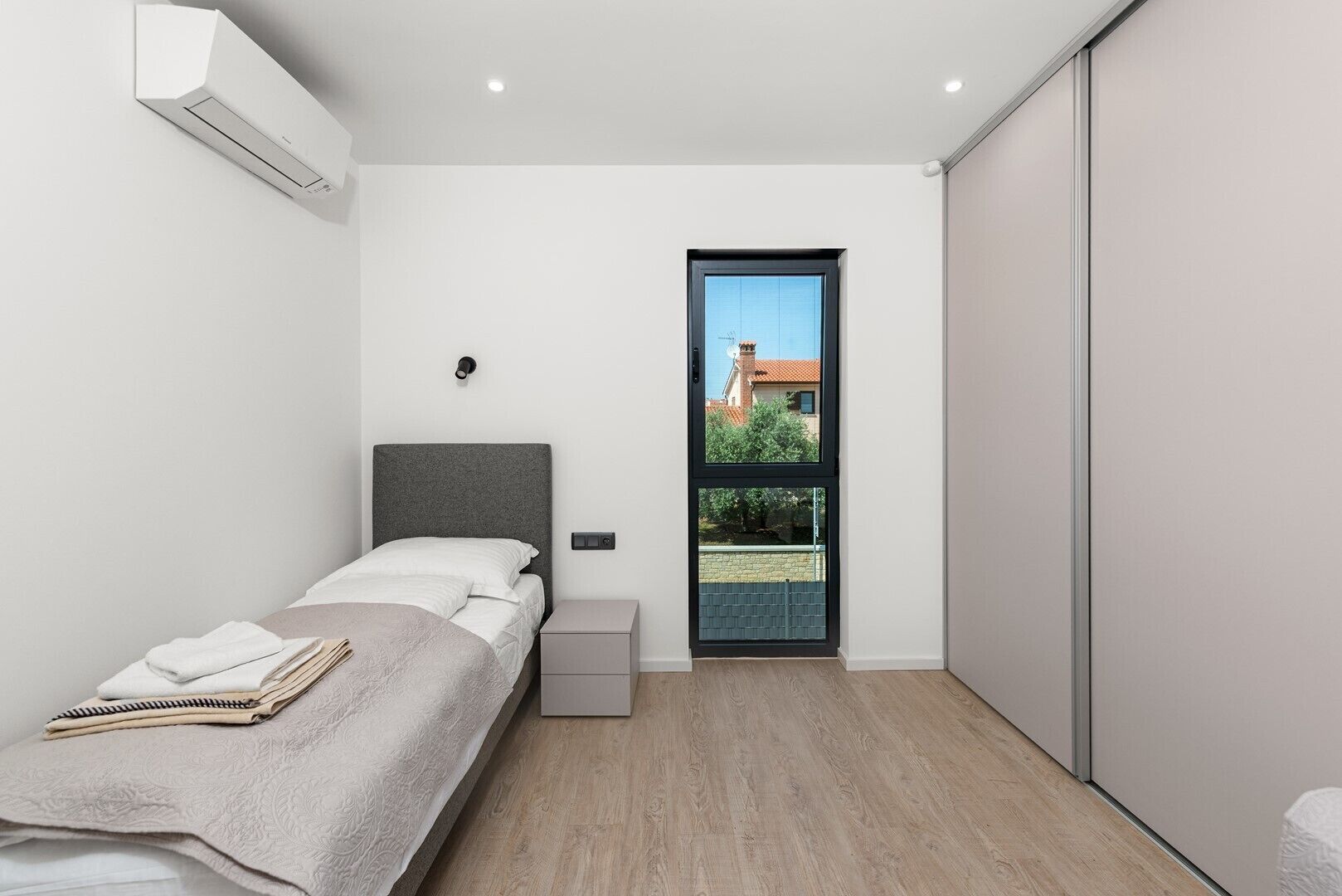 A modern bedroom with a bed, bedside table, and a view of the outside.