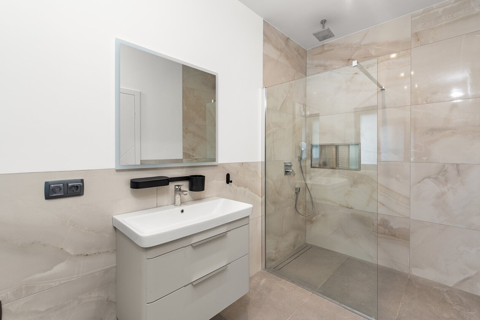 A modern bathroom with a glass-enclosed shower, a white sink, and a mirror above the sink.