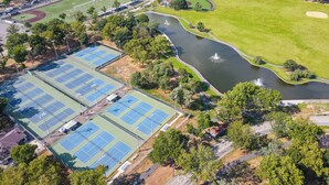 Vue aérienne d’un complexe sportif comprenant plusieurs courts de tennis, un parcours de golf et un lac agrémenté de fontaines.