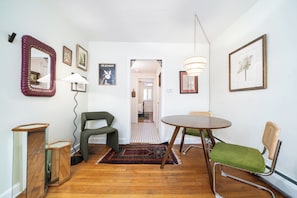 A dining area with a round table, two chairs, a patterned rug, and a mirror on the wall.