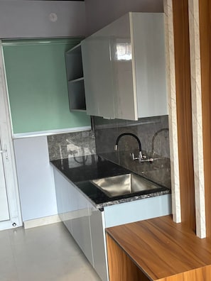 Cozinha com bancada preta, pia de aço inoxidável e armários brancos.