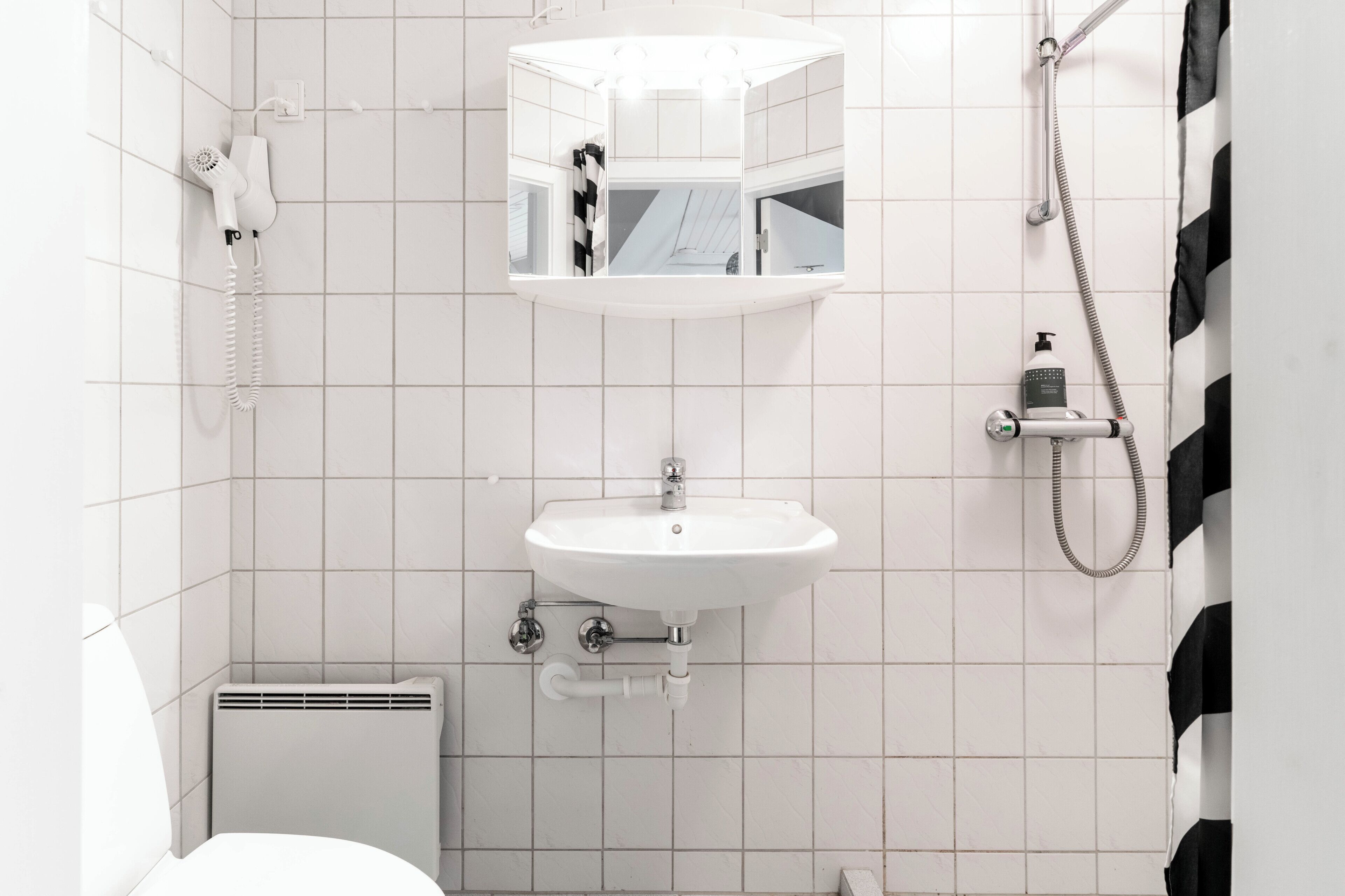 Un baño con lavamanos blanco, espejo, ducha y secador de pelo.