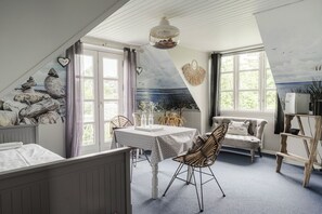 Ett rum med ett sluttande tak, ett matbord med stolar, en soffa, en dekorativ väggmålning och ett stort fönster.