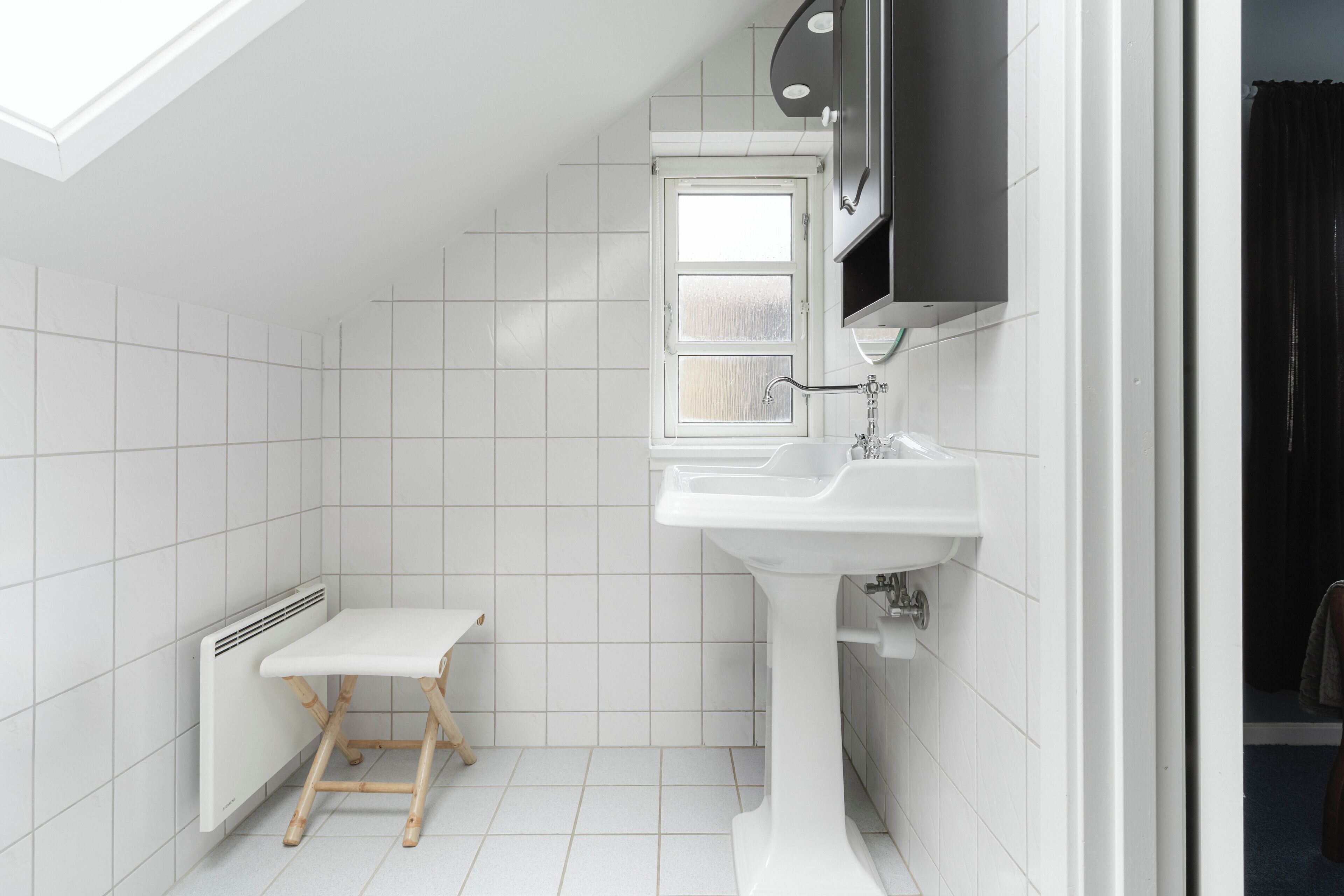 A small, white bathroom with a window, a white sink, and a radiator.