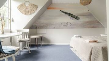 A bedroom with a sloped ceiling, a bed with a quilted cover, a chair, a small table, and a wall mural.