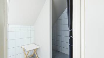 A small, narrow bathroom with white and gray tiles, a white bench, and a black shower curtain.