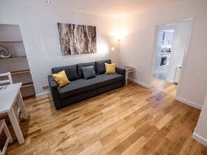 En moderne stue med en grå sofa, trægulv, et væghængt abstrakt maleri og et spiseområde med et hvidt bord og stole.