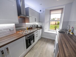 A modern kitchen with white cabinetry, a built-in oven, and a window overlooking a garden.