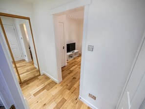 A room with wooden flooring, a television on a stand, and a door leading to another room.