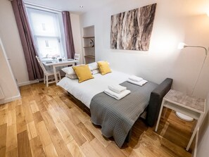 A bedroom with a bed, bedside table, chair, and a desk.