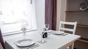 Uma mesa de jantar posta com pratos, talheres e copos de vinho, com uma janela e cortinas ao fundo.