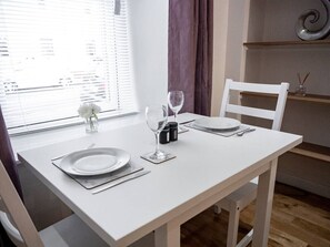 Et spisebord dækket med tallerkener, bestik og vinglas, med et vindue og gardiner i baggrunden.