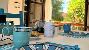 Uma mesa posta para o café da manhã, com chaleira, xícara e croissant, com vista para o verde lá fora.