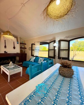 A living room with a sofa, a coffee table, a fireplace, and a large window with curtains. - Casa Antele, a relaxing retreat nestled between the garden and the sea in southern Sardinia  (Quartu Sant'Elena)