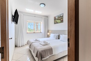 A hotel room with a bed, a window with curtains, a painting on the wall, and a flat-screen TV mounted on the wall. - #396 Perfect Vacation Apartment Near the Beach (Albufeira)
