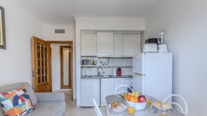 Una cocina compacta con armarios blancos, un tostador, una licuadora y una zona de comedor con una mesa dispuesta para el desayuno.