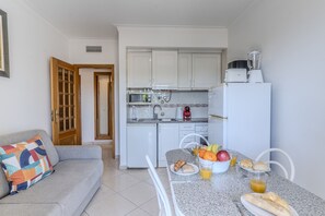 A compact kitchen with white cabinets, a toaster, a blender, and a dining area with a table set for breakfast. - #396 Perfect Vacation Apartment Near the Beach (Albufeira)