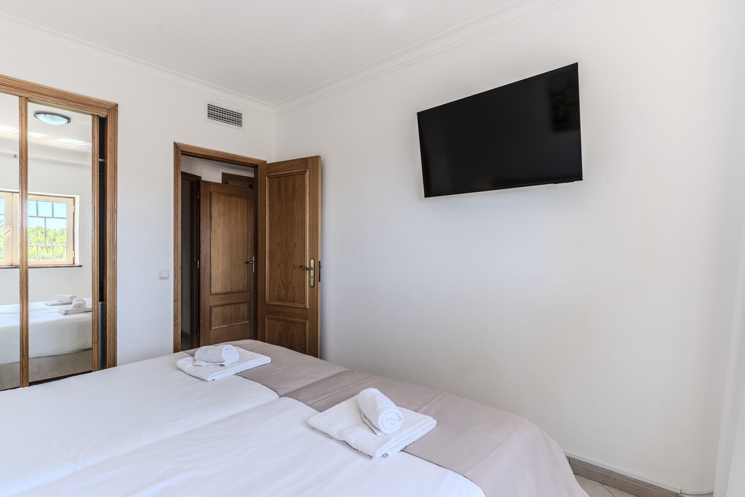 Quarto de hotel com uma cama, uma TV fixada na parede e uma porta que dá para outro quarto.