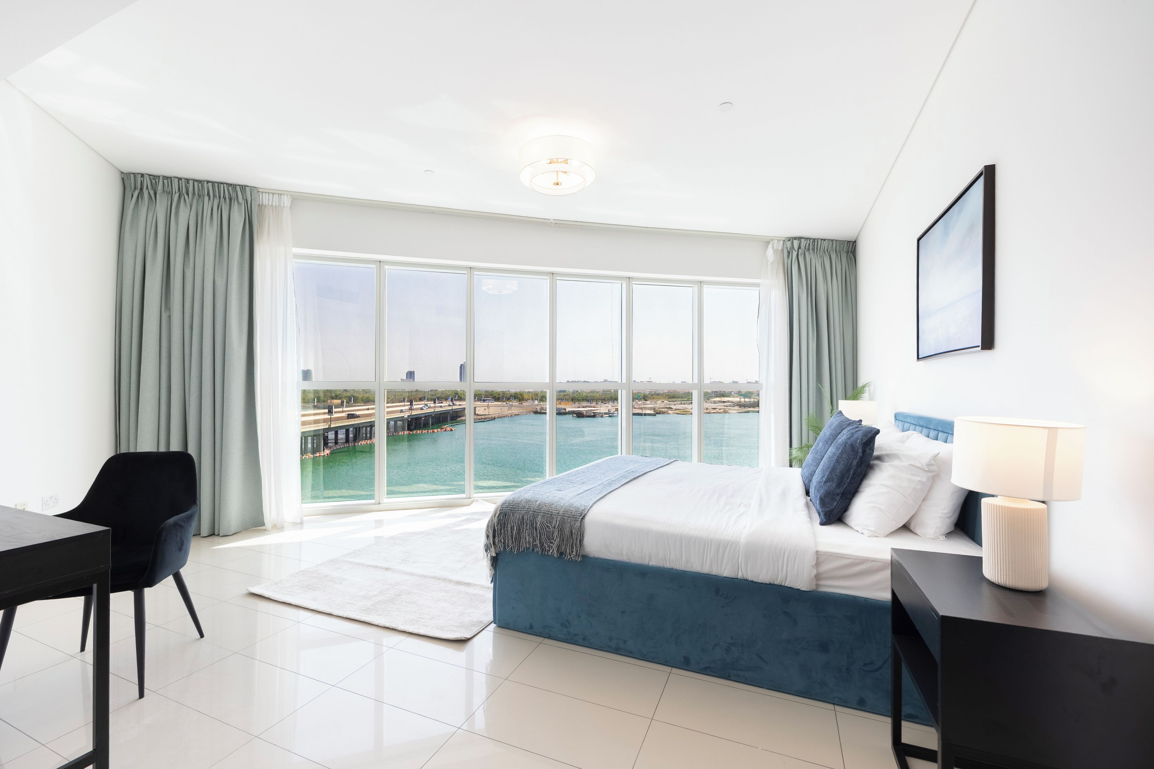 A modern hotel room with a large window, a bed, a desk, and a chair.