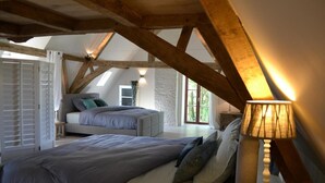 A bedroom with a large bed, a bedside table with a lamp, a window with a view, and exposed wooden beams. - Holiday home Bellefleur (Houtem Veurne)