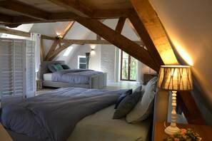 Ein Schlafzimmer mit einem großen Bett, einem Nachttisch mit Lampe, einem Fenster mit Ausblick und freiliegenden Holzbalken.