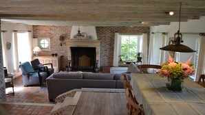 A rustic living room with a fireplace, a dining table with a vase of flowers, and a brick wall. - Holiday home Bellefleur (Houtem Veurne)