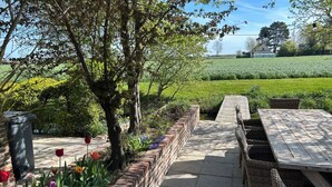A patio area with a brick planter, wicker furniture, and a view of a green field. - Holiday home Bellefleur (Houtem Veurne)