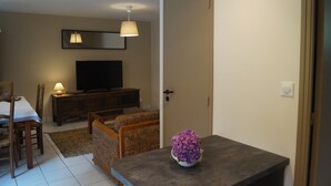 A living room with a television, a sofa, a dining table with chairs, a lamp, and a door.