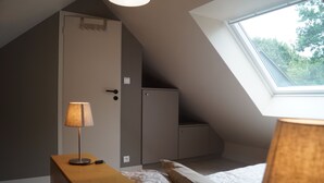 A bedroom with a sloped ceiling, a skylight, a bed with pillows, a bedside table with a lamp, and a wardrobe.