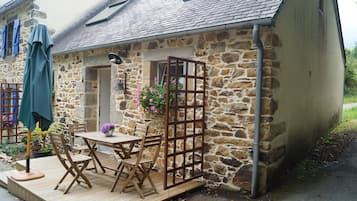 Un bâtiment en pierre doté d’une terrasse en bois, d’une table avec des chaises et d’un panier à fleurs suspendu.