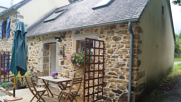A stone building with a wooden deck, a table with chairs, and a hanging flower basket. - A small house in the countryside (Plougastel-Daoulas)