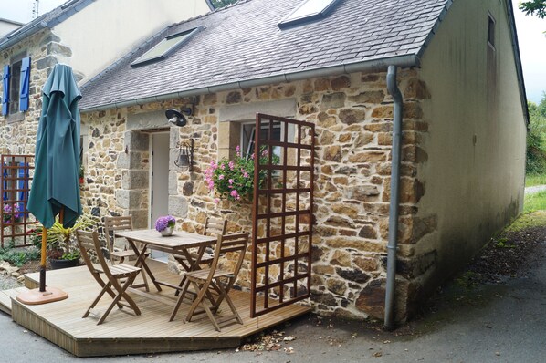 Un edificio de piedra con una terraza de madera, una mesa con sillas y una cesta colgante de flores.